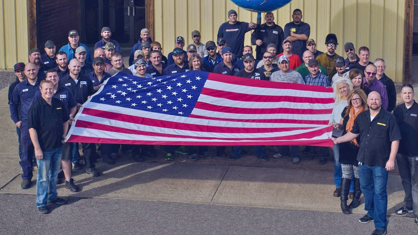 Andersen Hitches employees gathered outside around a large American flag, representing American-made craftsmanship.