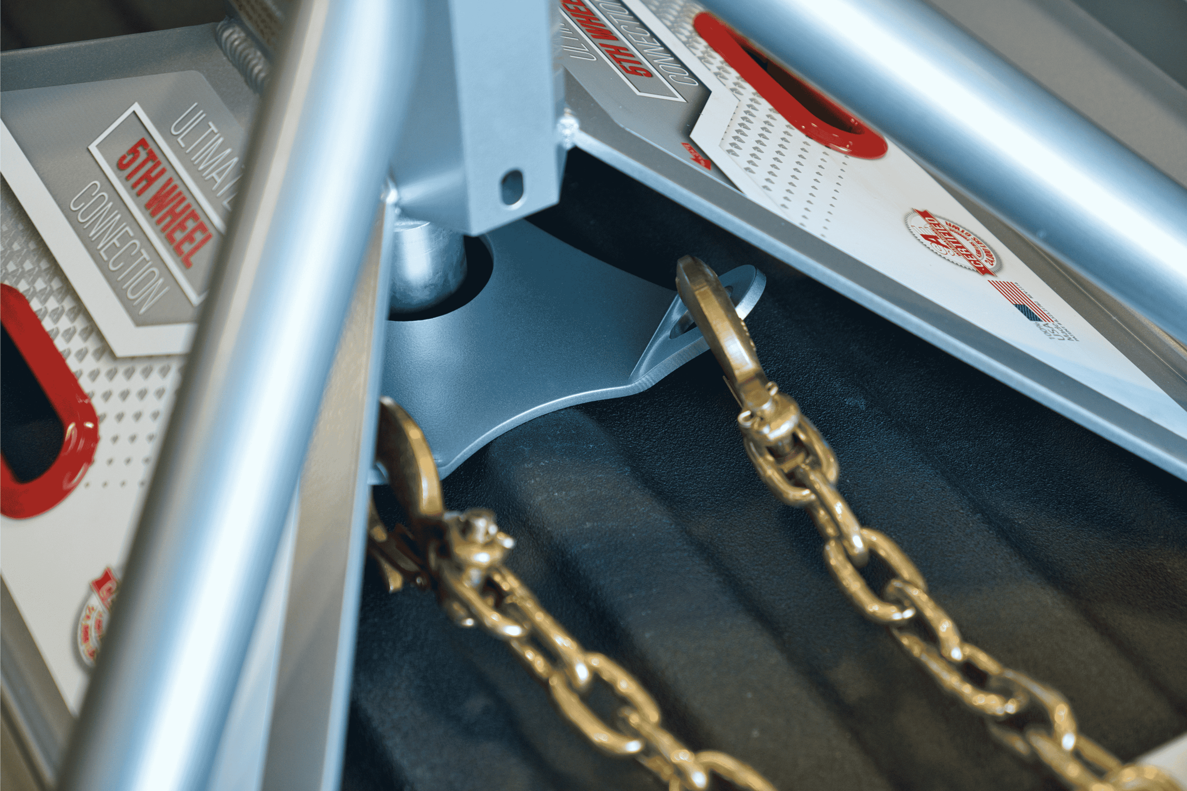 Close-up of the Andersen Hitches Safety Chains with Plate (#3249) installed on the Ultimate 5th Wheel Connection gooseneck mount. The image highlights the heavy-duty Grade 70 safety chains, rated at 18,000 lbs each, connected to a specialized base plate designed for easy installation and enhanced towing security in a truck bed with a spray-in liner.