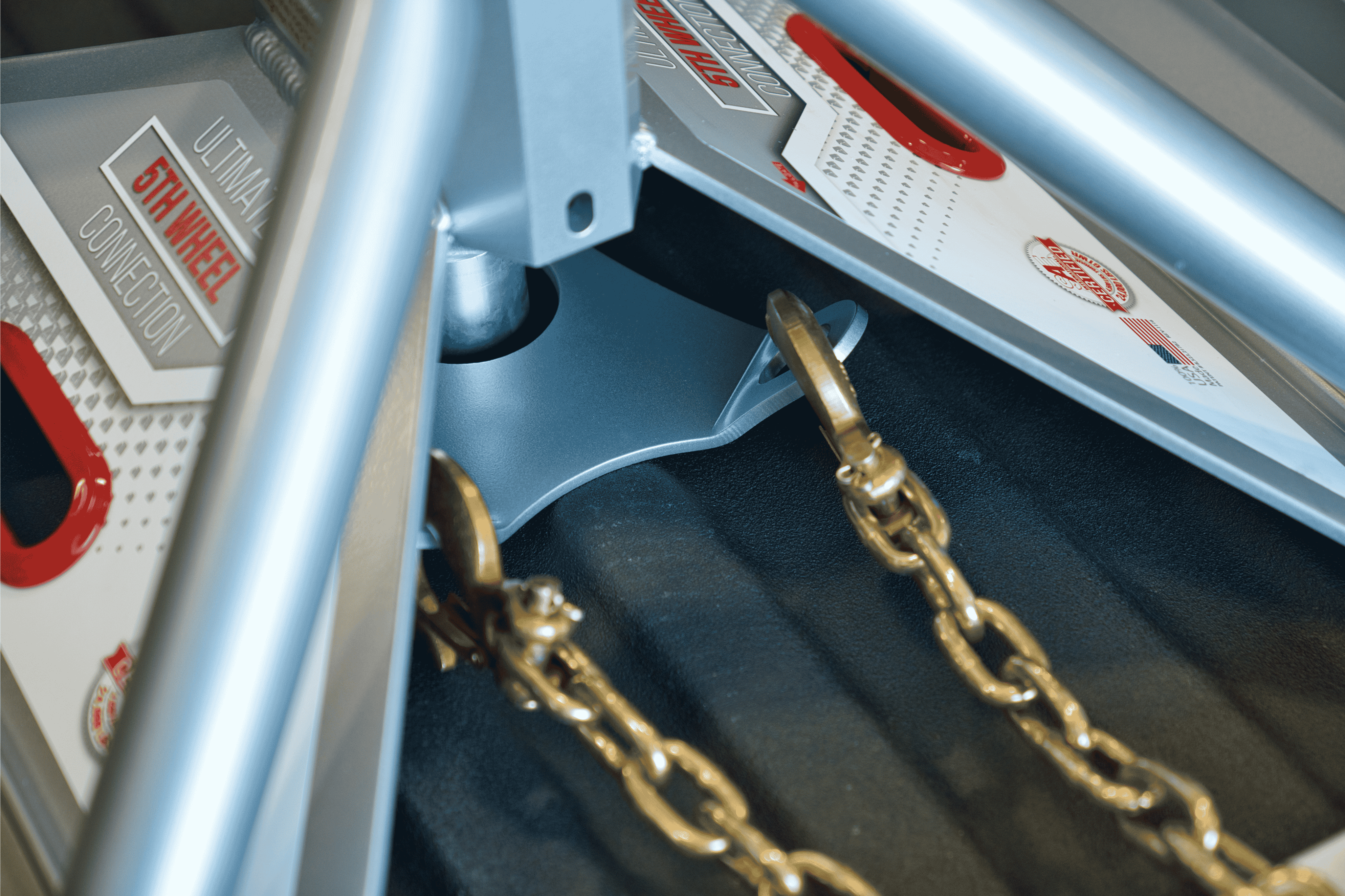 Close-up of the Andersen Hitches Safety Chains with Plate (#3249) installed on the Ultimate 5th Wheel Connection gooseneck mount. The image highlights the heavy-duty Grade 70 safety chains, rated at 18,000 lbs each, connected to a specialized base plate designed for easy installation and enhanced towing security in a truck bed with a spray-in liner.